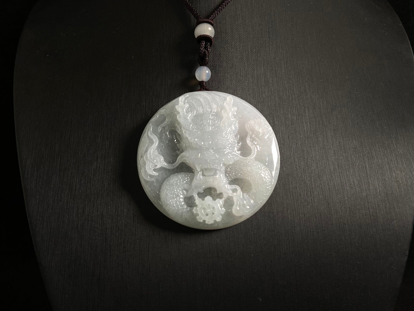 This exquisite pendant features a circular milky white jade disc intricately carved with a majestic dragon head design.