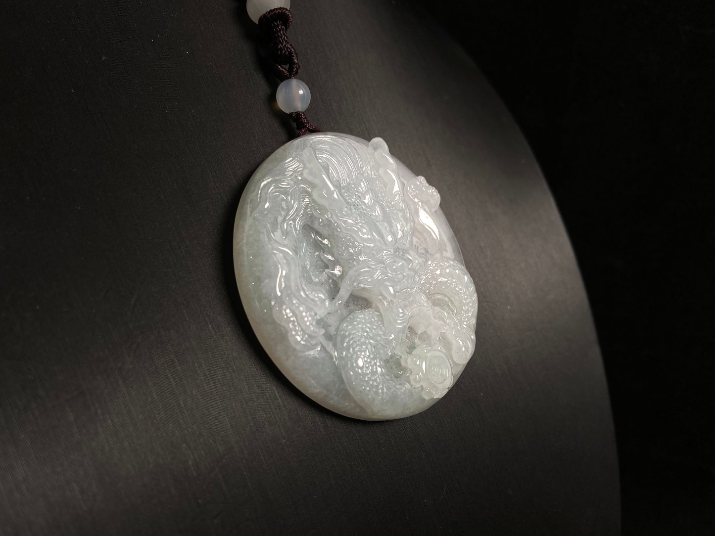 This exquisite pendant features a circular milky white jade disc intricately carved with a majestic dragon head design.
