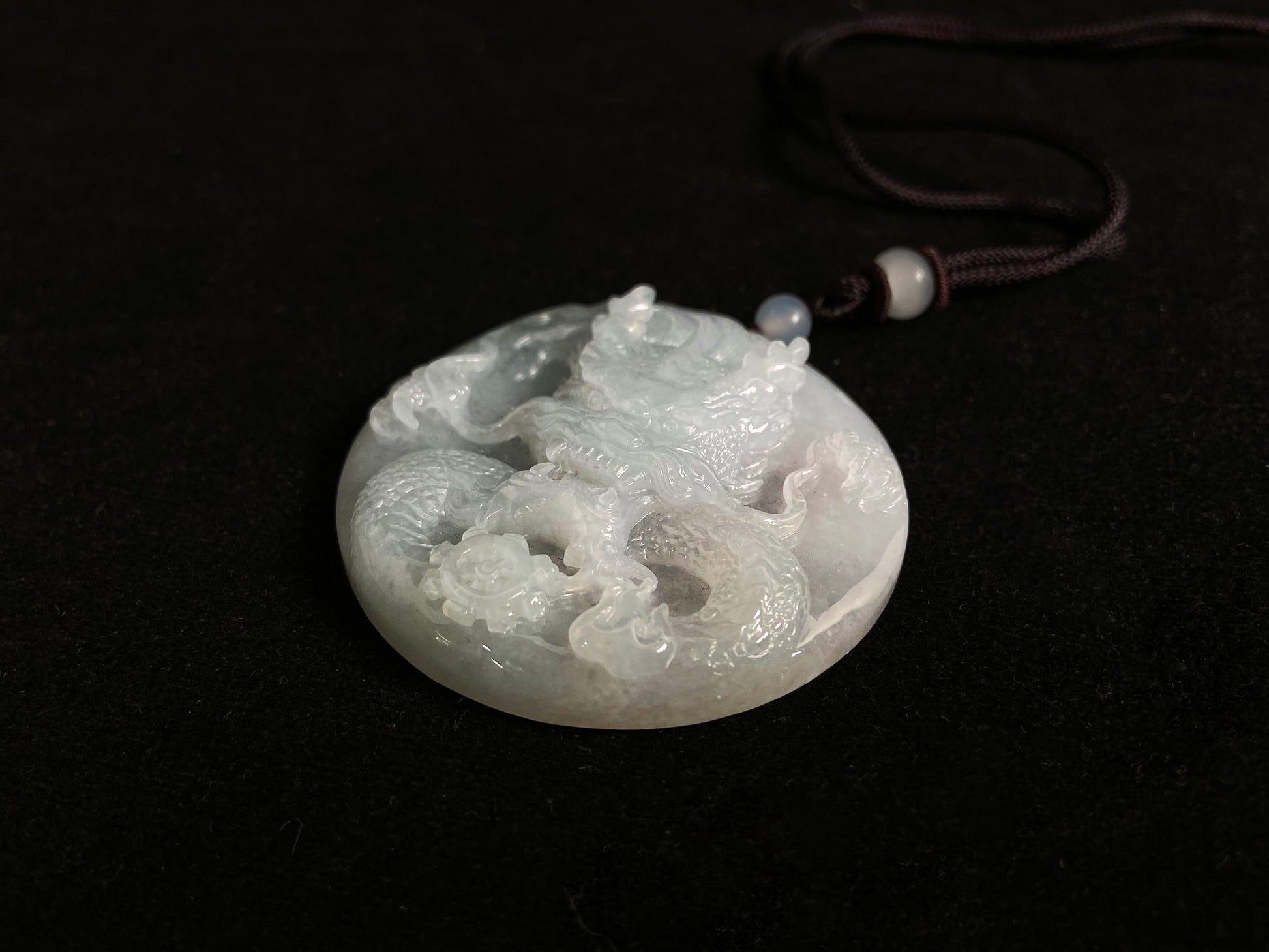 This exquisite pendant features a circular milky white jade disc intricately carved with a majestic dragon head design.