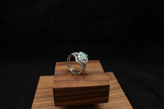 Silver ring with a green gemstone on a wooden stand against a black background