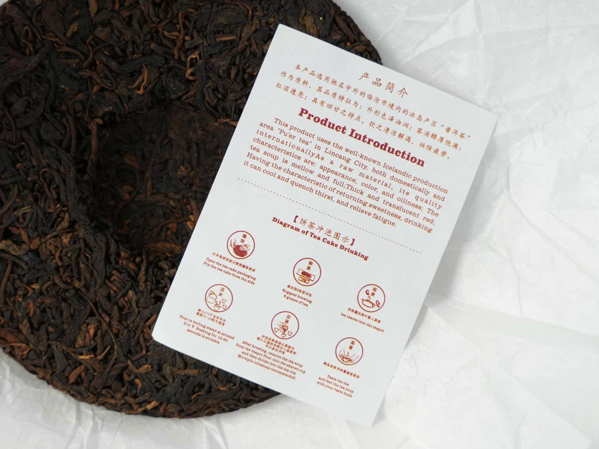 A top-down view of a Bingdao ripe Pu-erh tea cake, with a instruction sheet placed on its surface, printed with product details and step-by-step brewing guidelines.