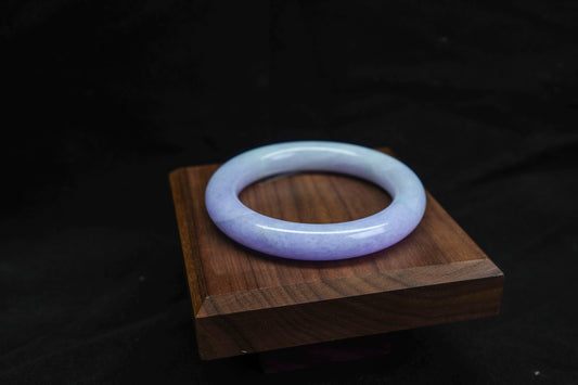 Translucent purple jade bracelet on a wooden stand against a dark background