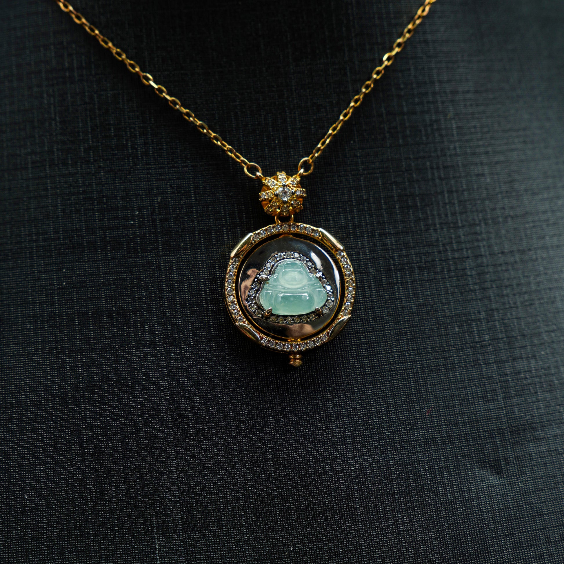 Gold necklace with a pendant featuring a green gemstone on a black fabric background