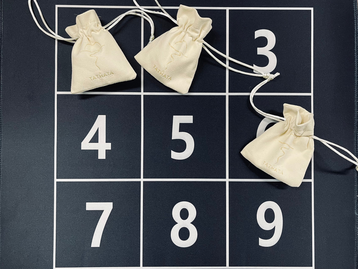 Nine white drawstring bags numbered 3 to 9 on a black grid background