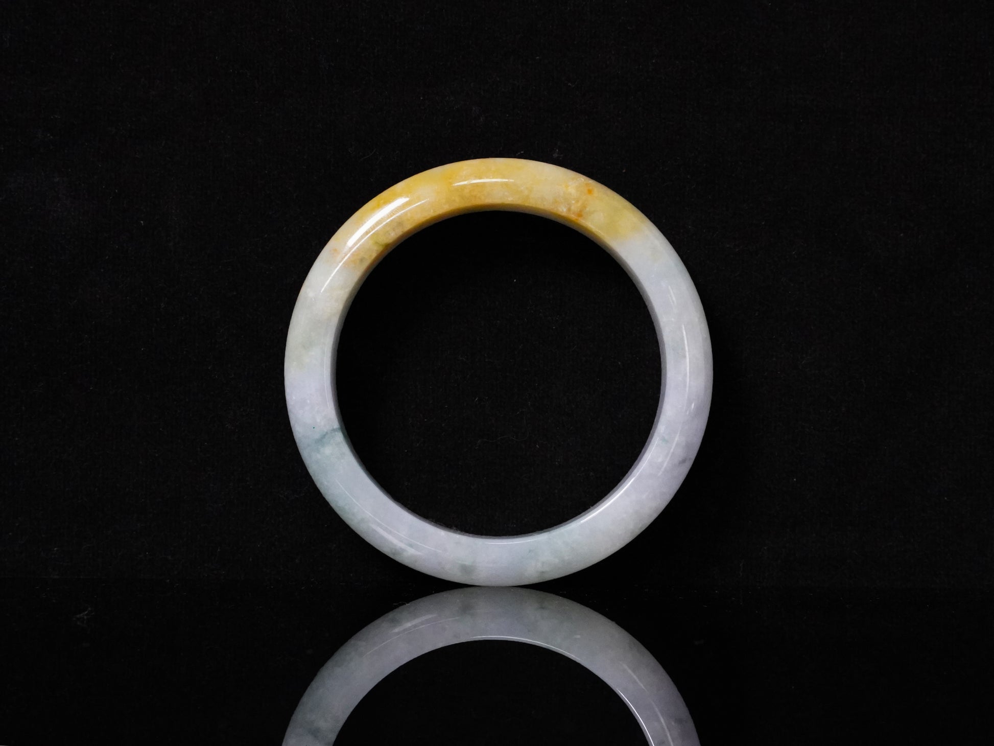 This jadeite bangle has a white base with floating green and honey-yellow hues.