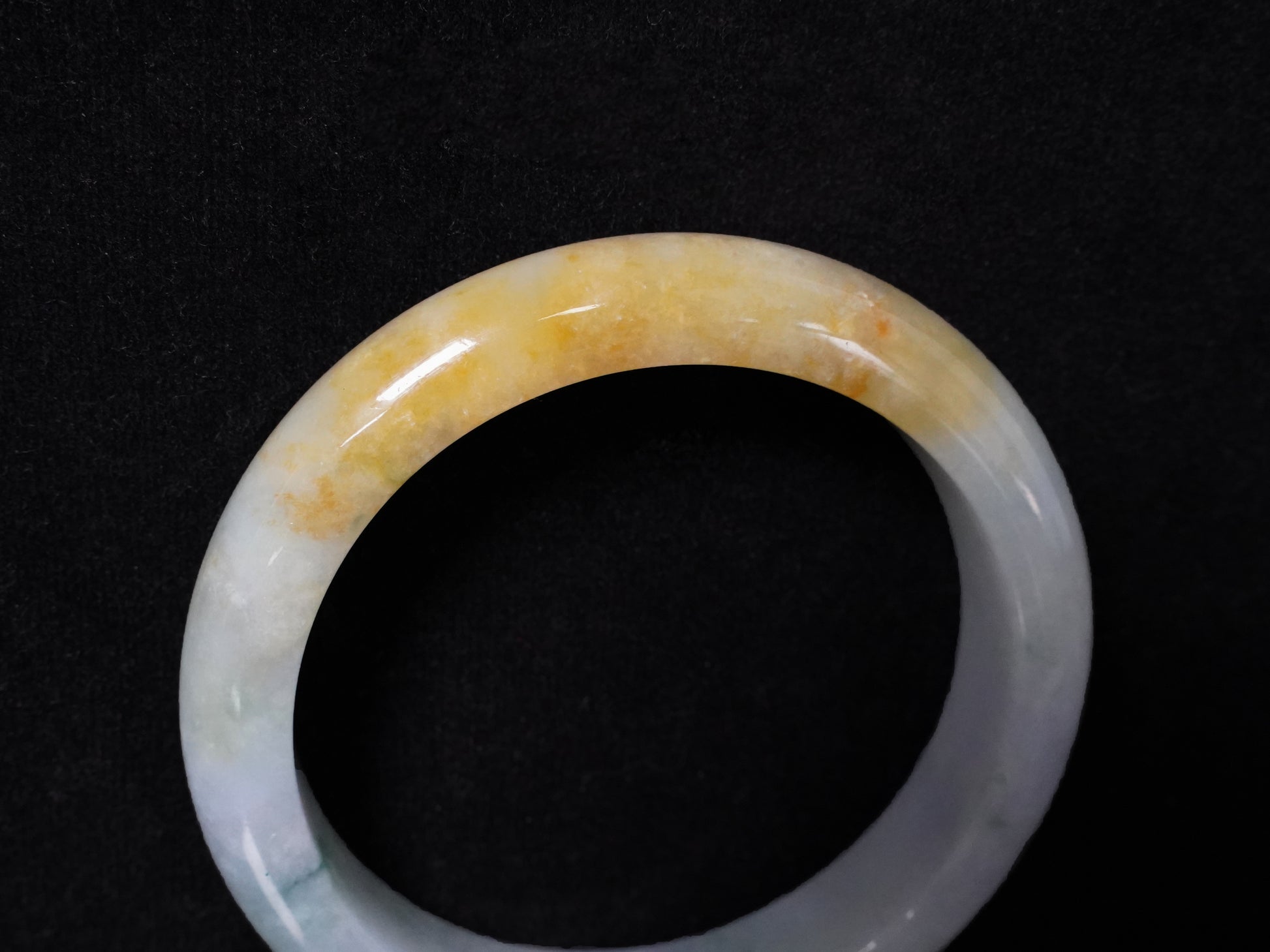 This jadeite bangle has a white base with floating green and honey-yellow hues.