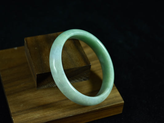 Green jade bracelet on a wooden stand with a dark background
