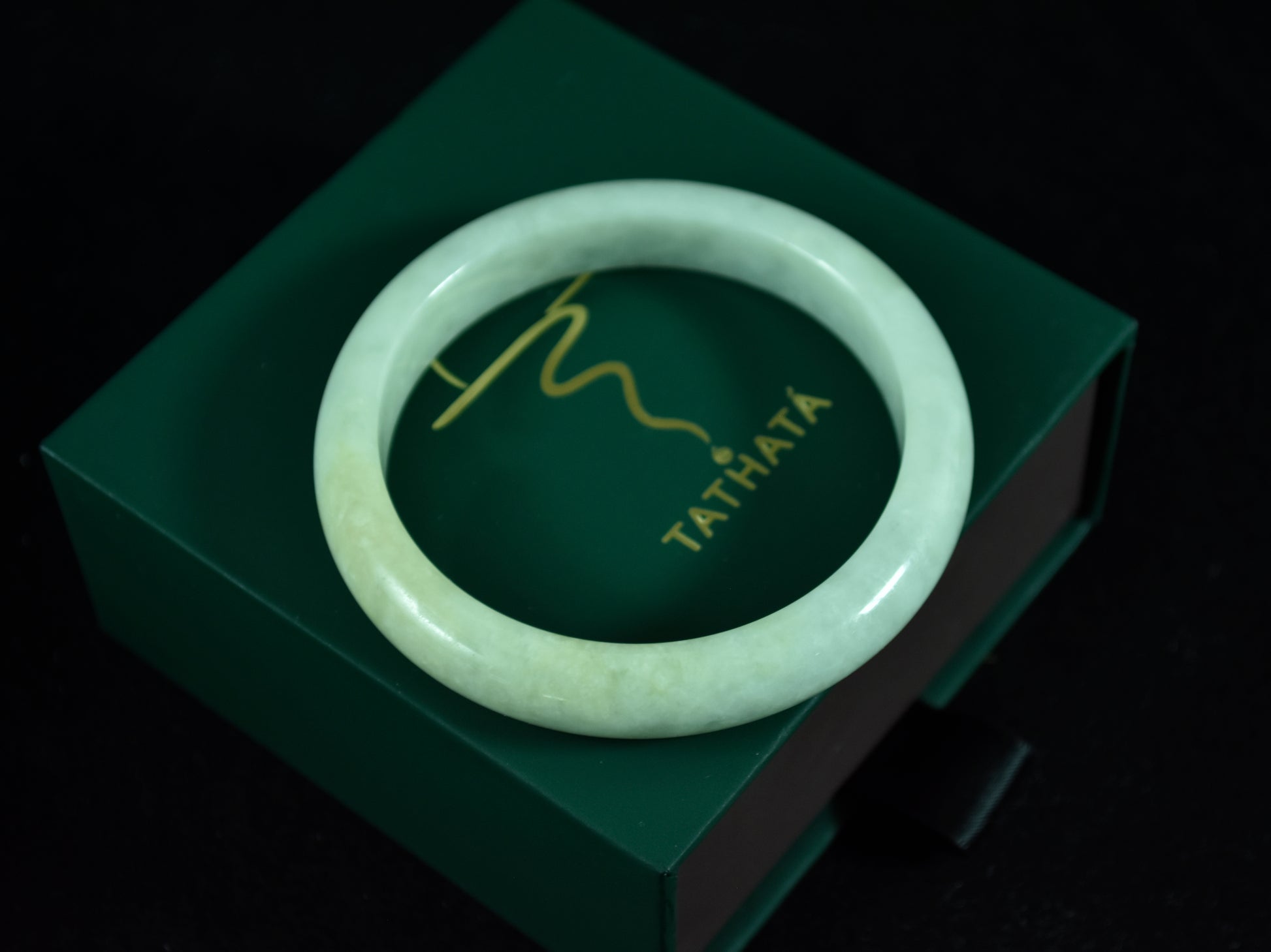 Green jade bracelet on a green box with 'TATHATA' branding.