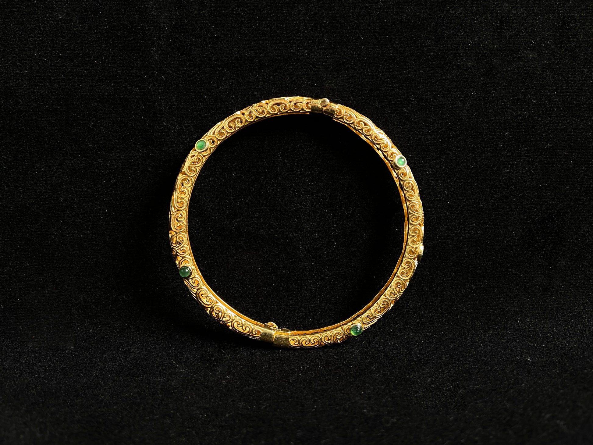 A gold plated openwork bangle with cloud motifs, set with nine light green jade beads.