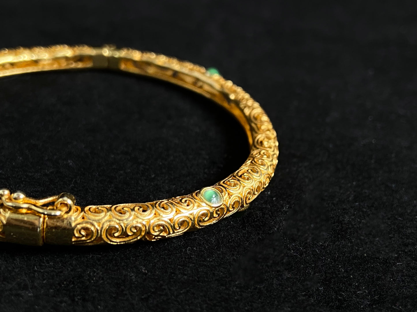 A gold plated openwork bangle with cloud motifs, set with nine light green jade beads.