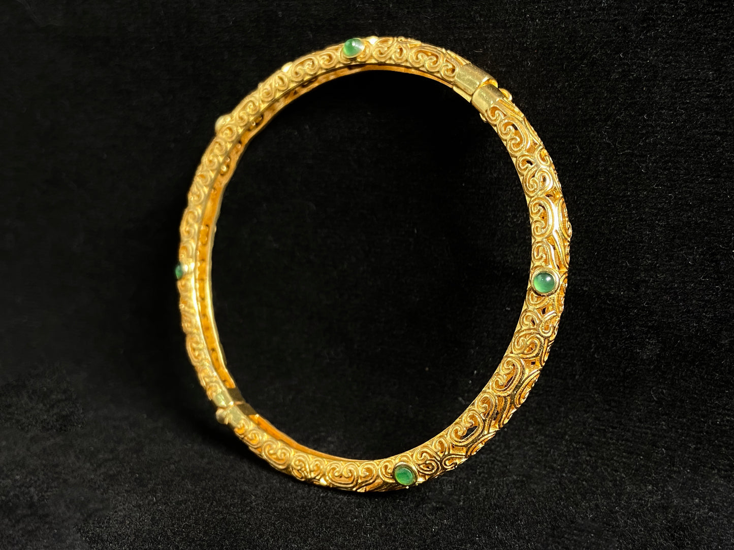 A gold plated openwork bangle with cloud motifs, set with nine light green jade beads.
