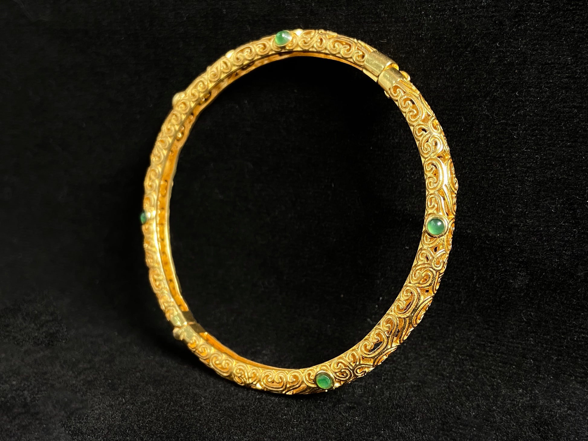 A gold plated openwork bangle with cloud motifs, set with nine light green jade beads.