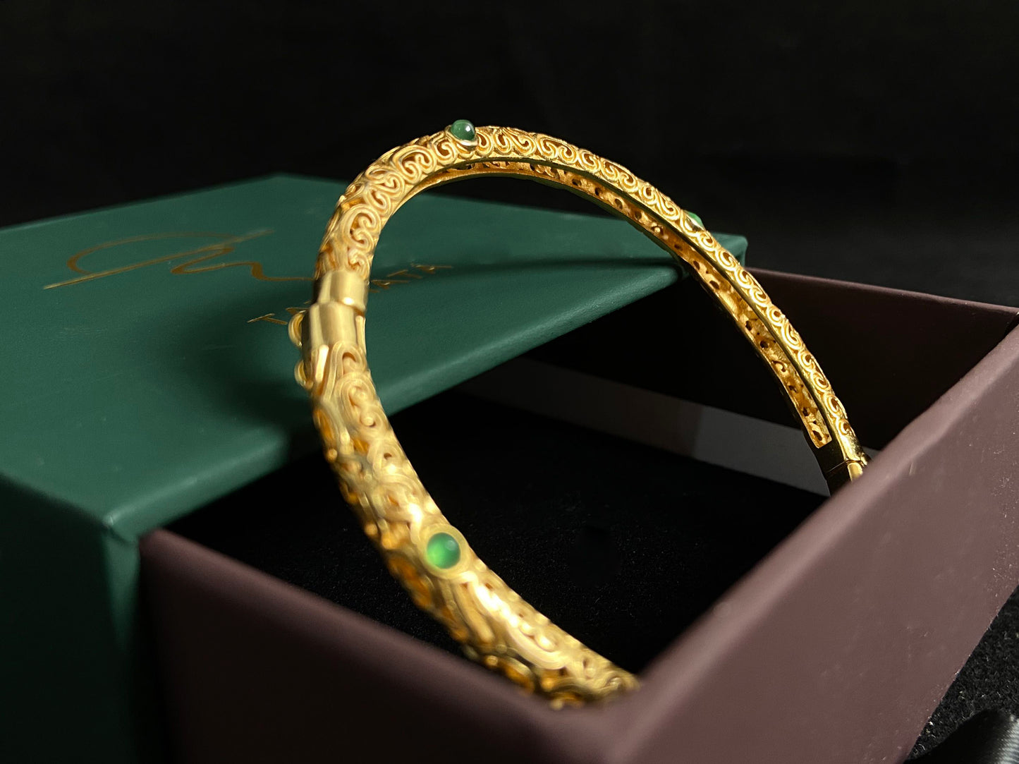 A gold plated openwork bangle with cloud motifs, set with nine light green jade beads.