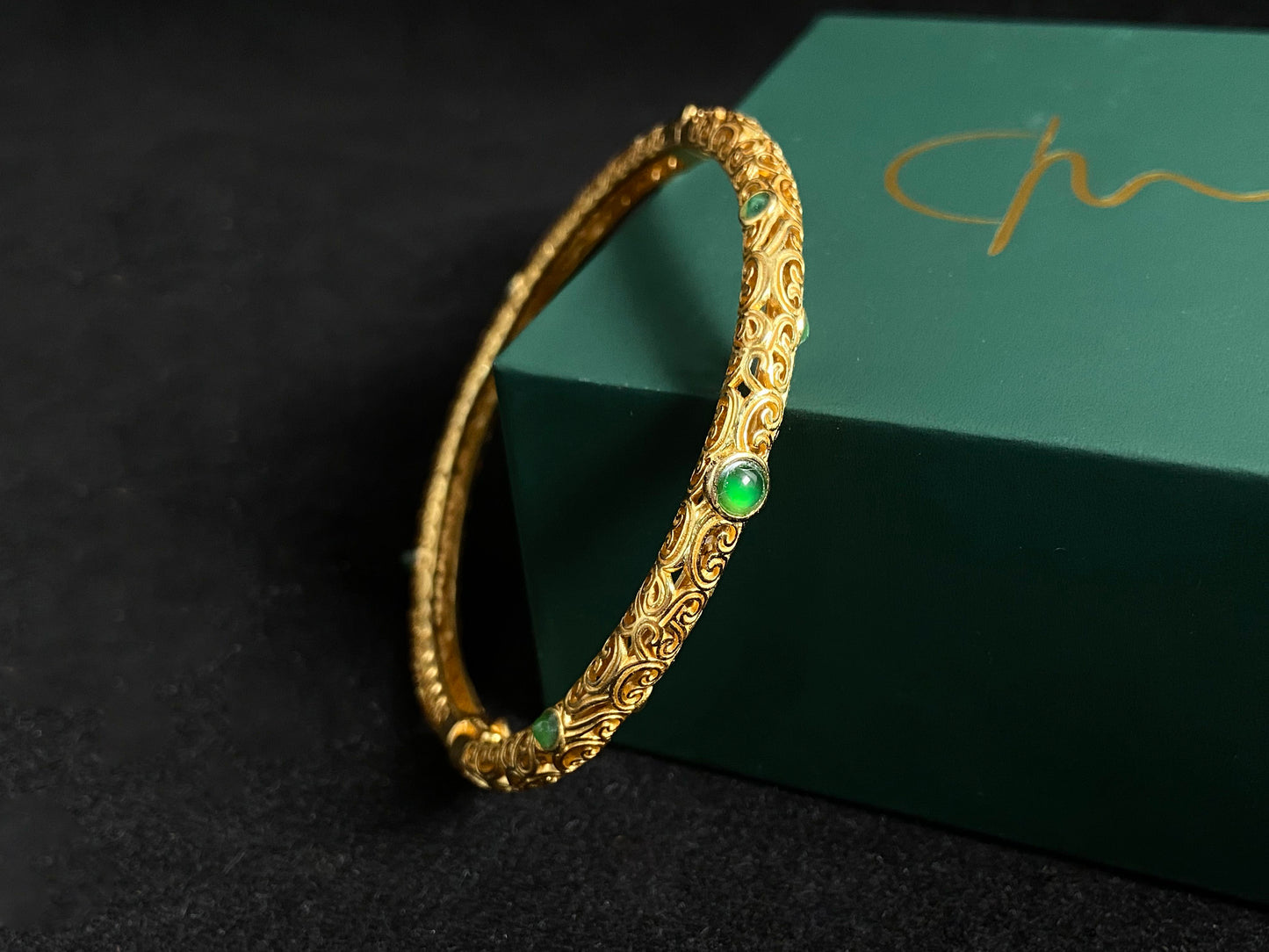 A gold plated openwork bangle with cloud motifs, set with nine light green jade beads.