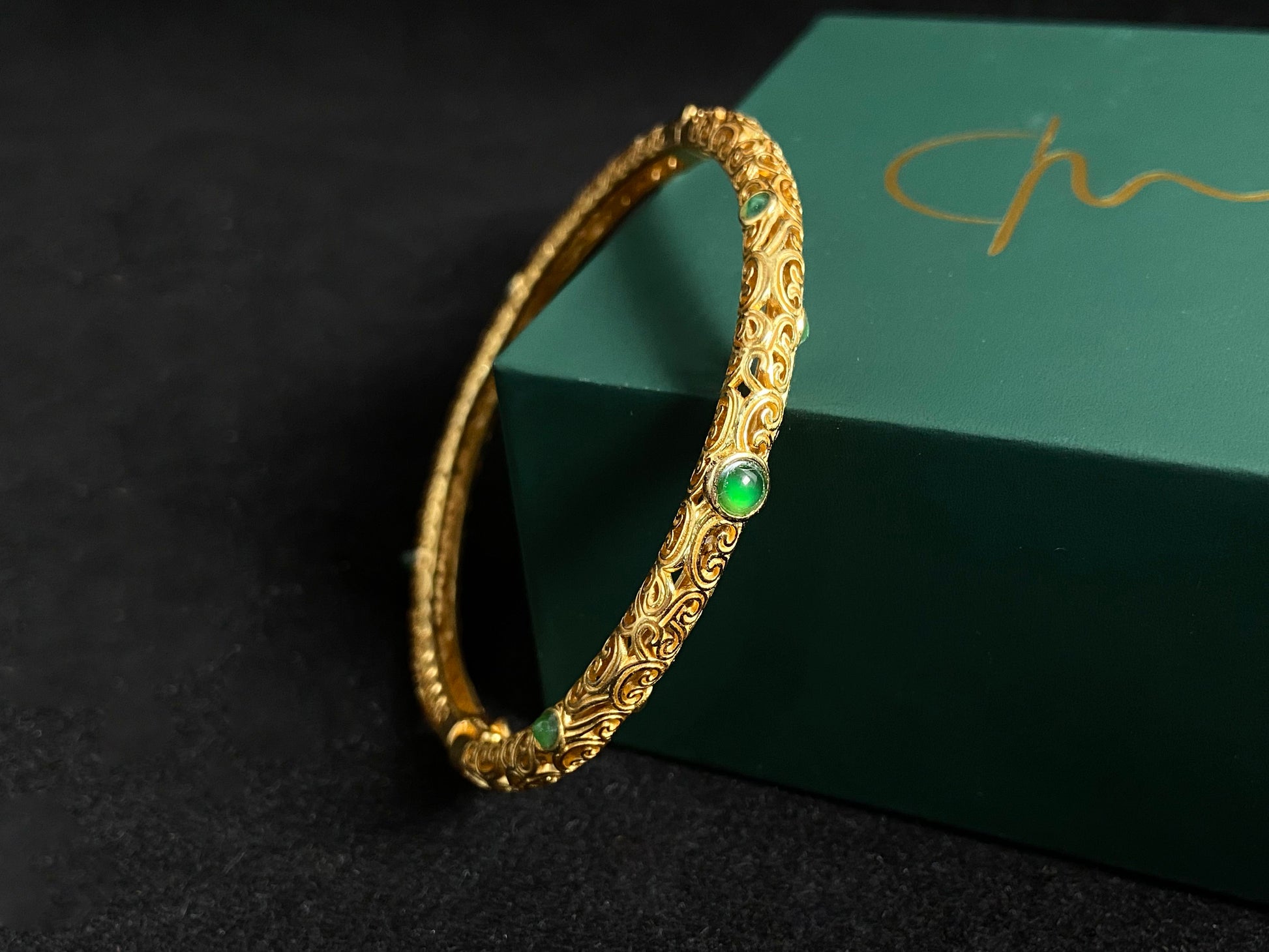 A gold plated openwork bangle with cloud motifs, set with nine light green jade beads.