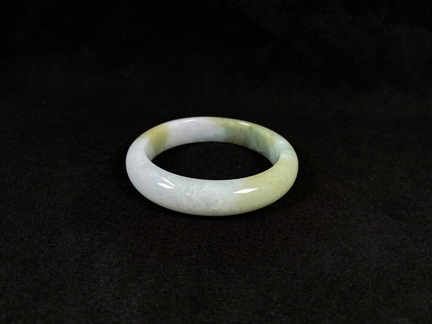 A creamy white jadeite bangle adorned with splashes of yellow-green.