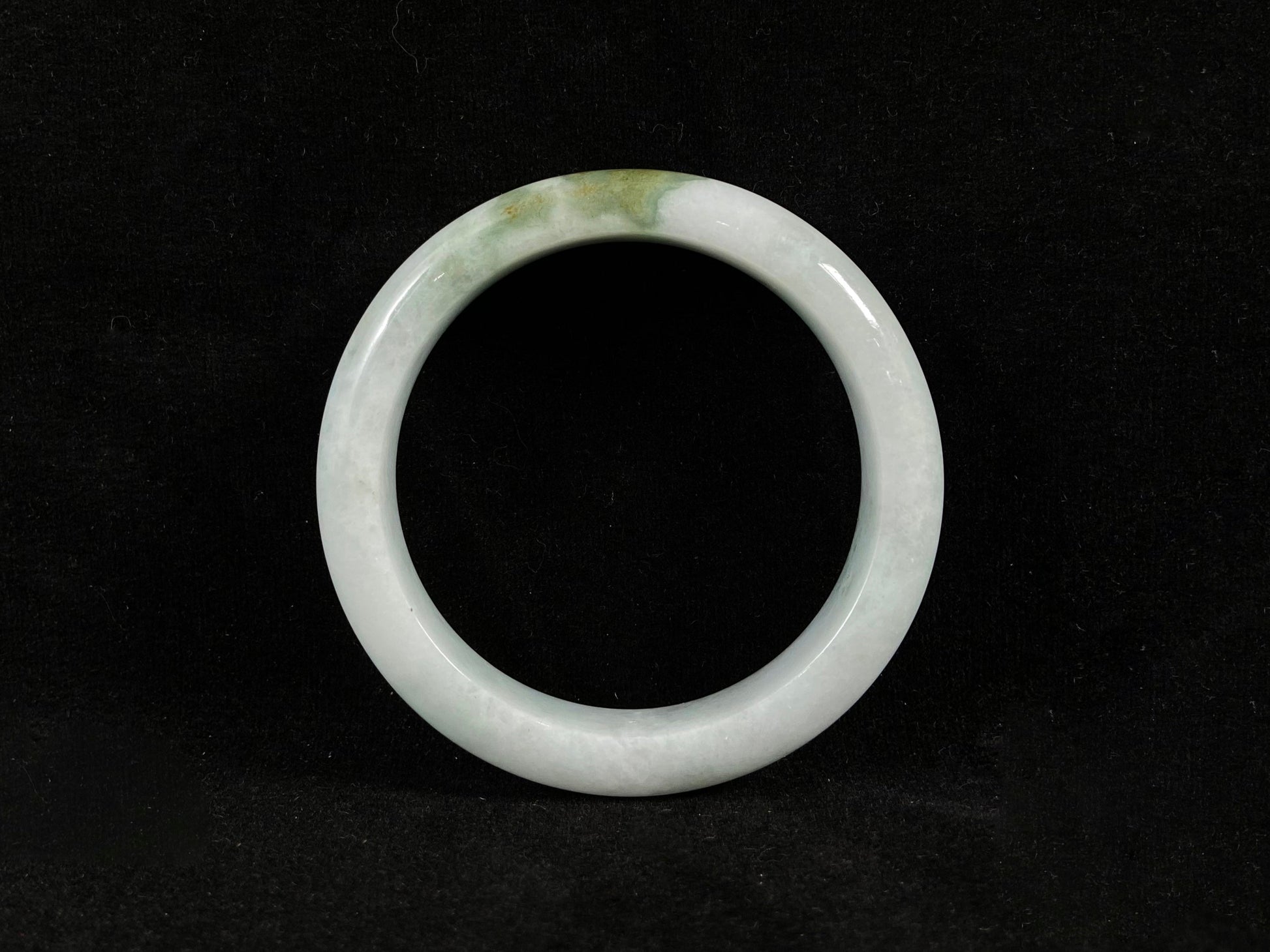 A pearl-white jade bangle embraced by a soft green mountain-water gradient.