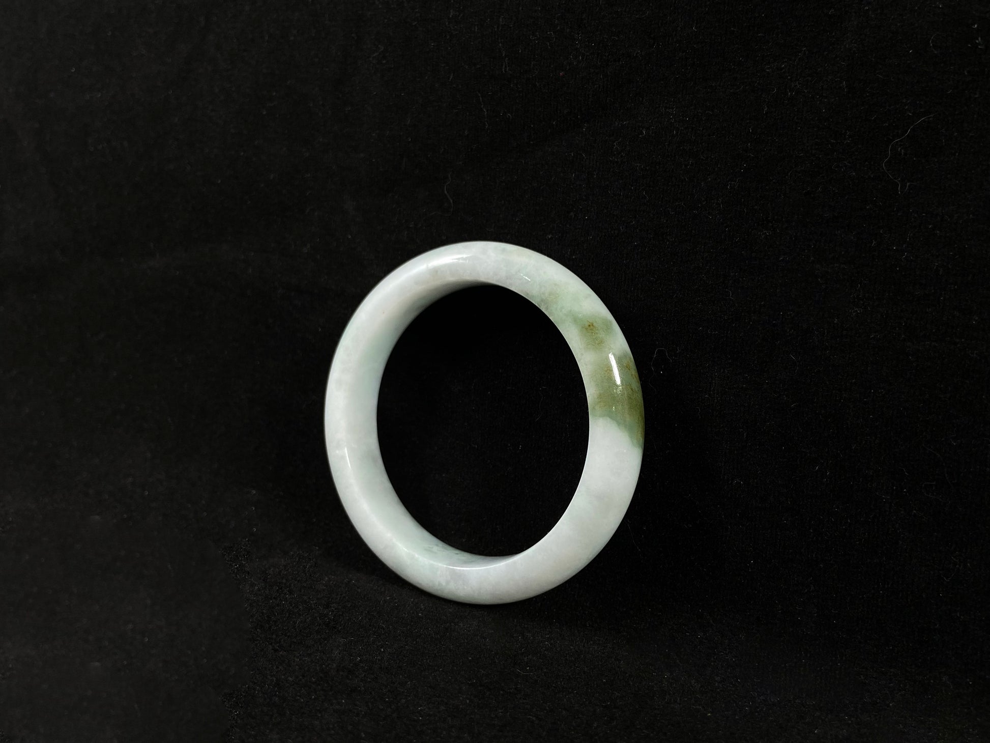 A pearl-white jade bangle embraced by a soft green mountain-water gradient.