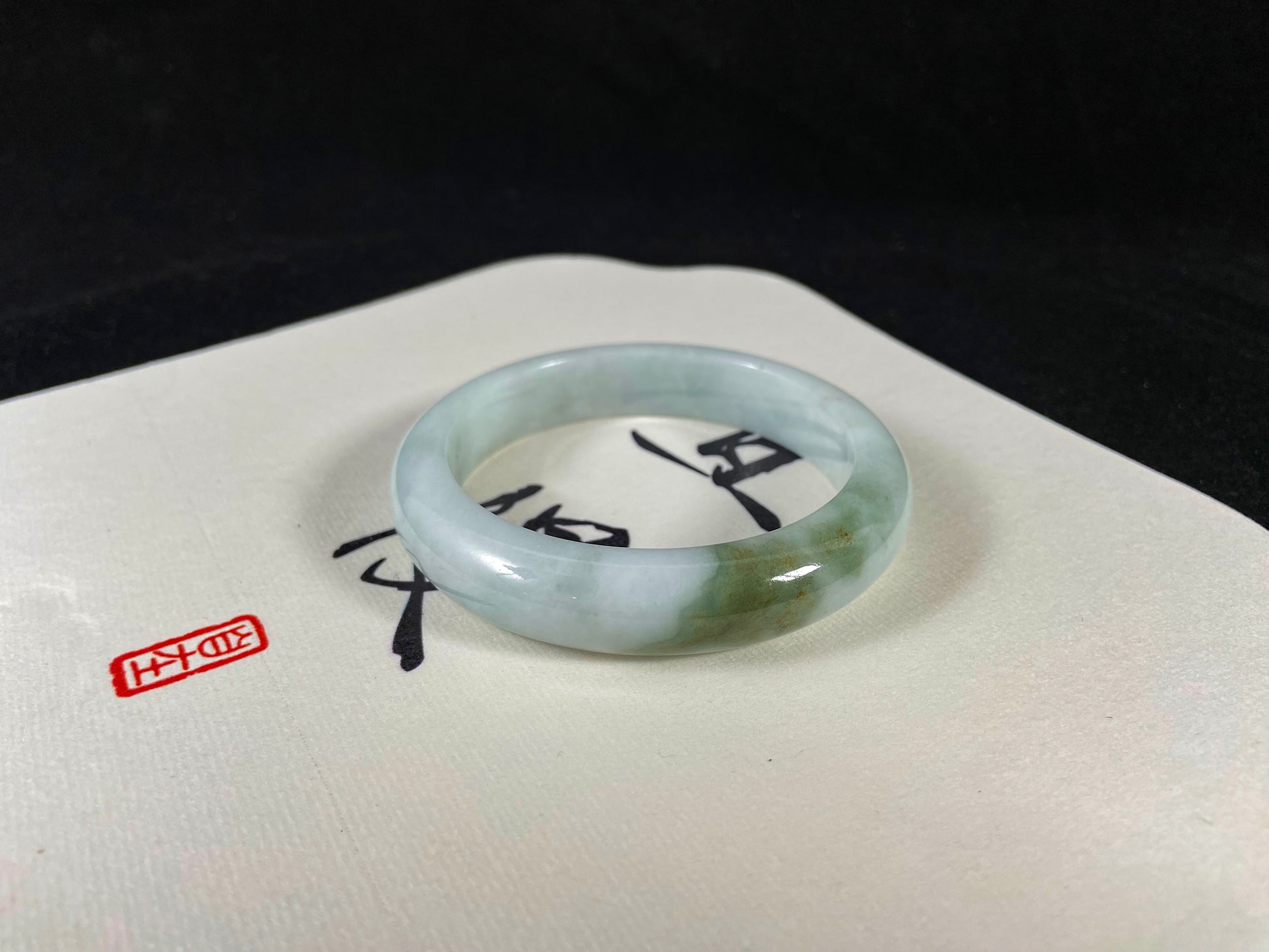 A pearl-white jade bangle embraced by a soft green mountain-water gradient.