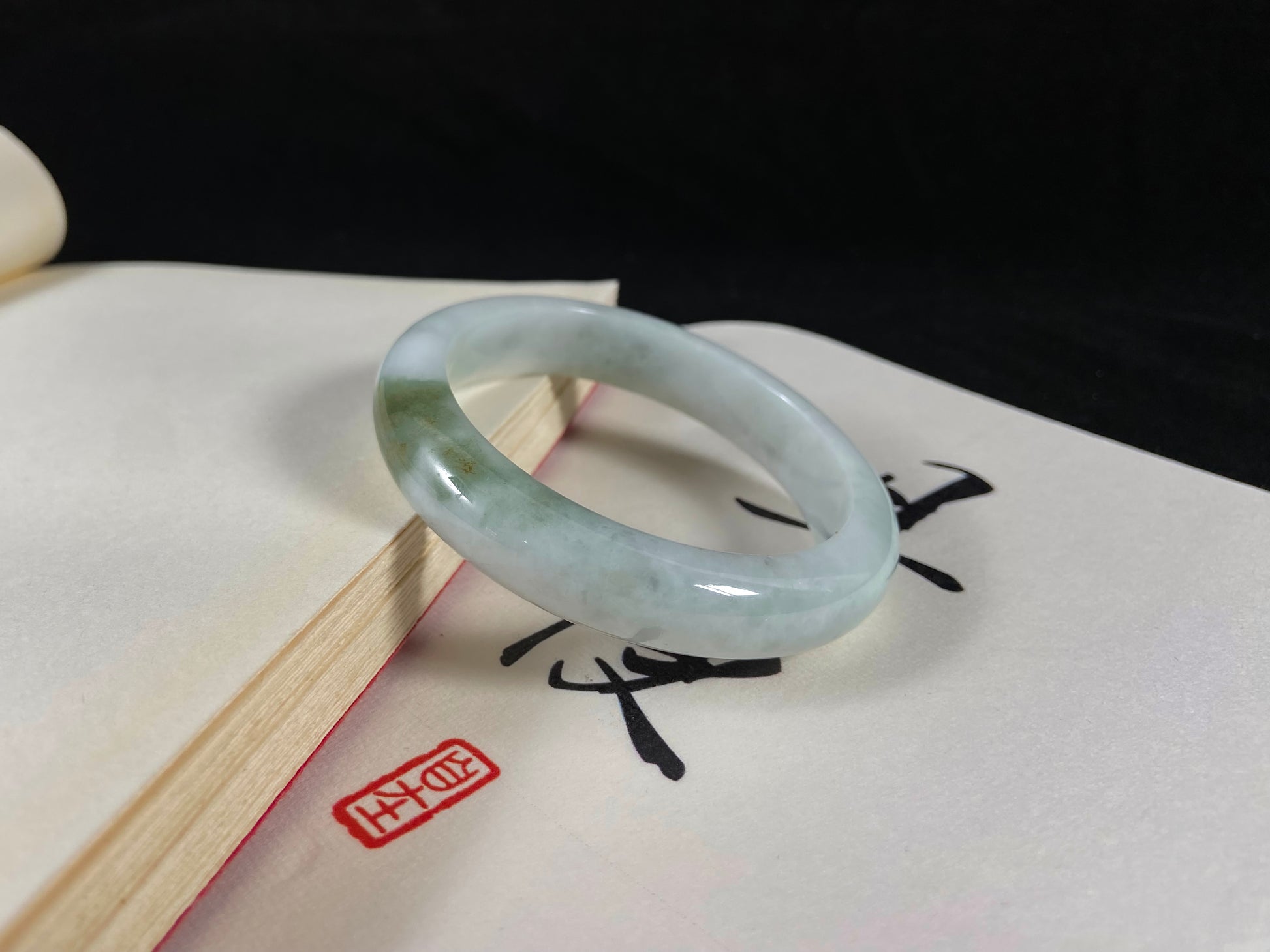 A pearl-white jade bangle embraced by a soft green mountain-water gradient.