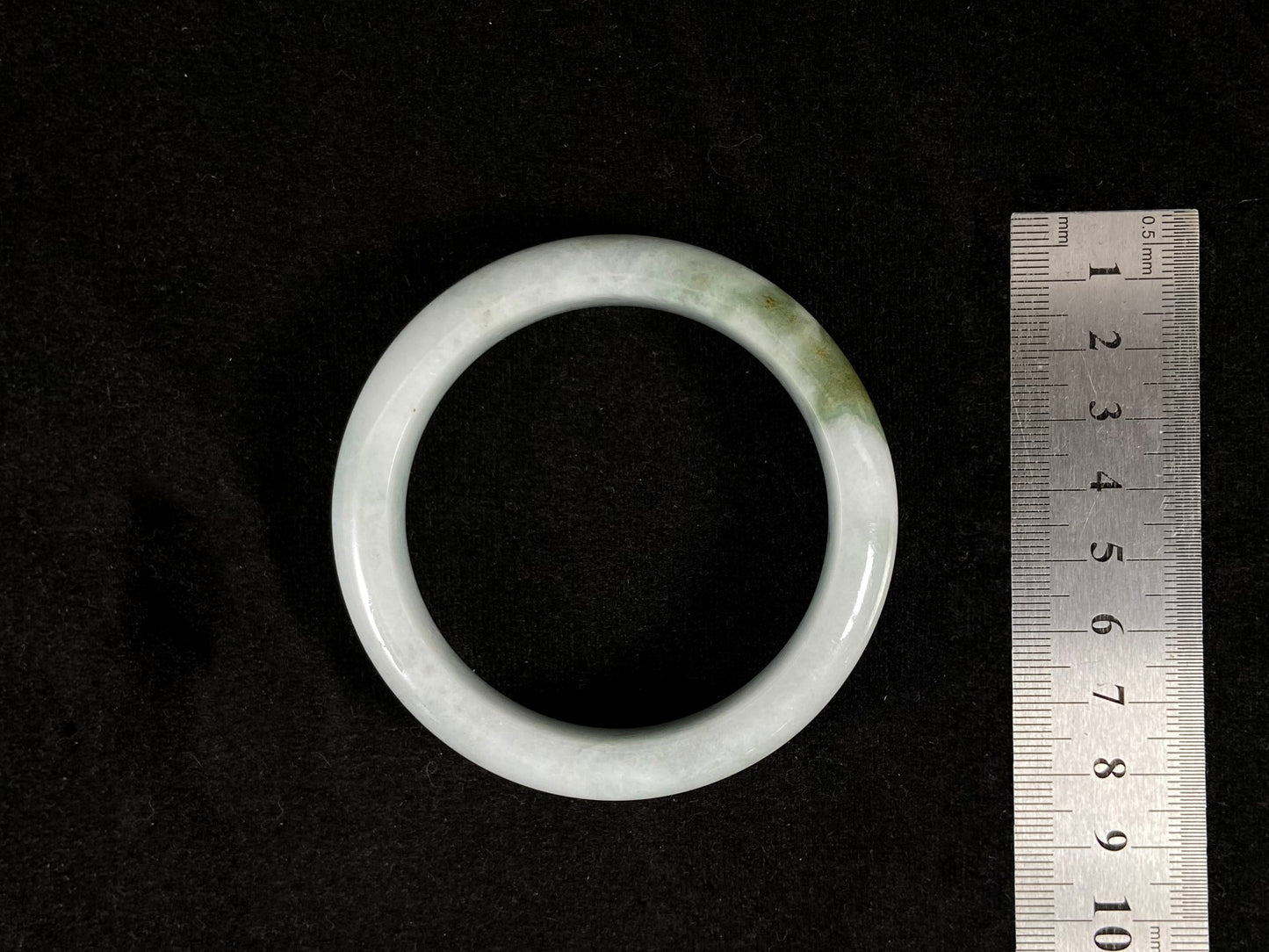 A pearl-white jade bangle embraced by a soft green mountain-water gradient.