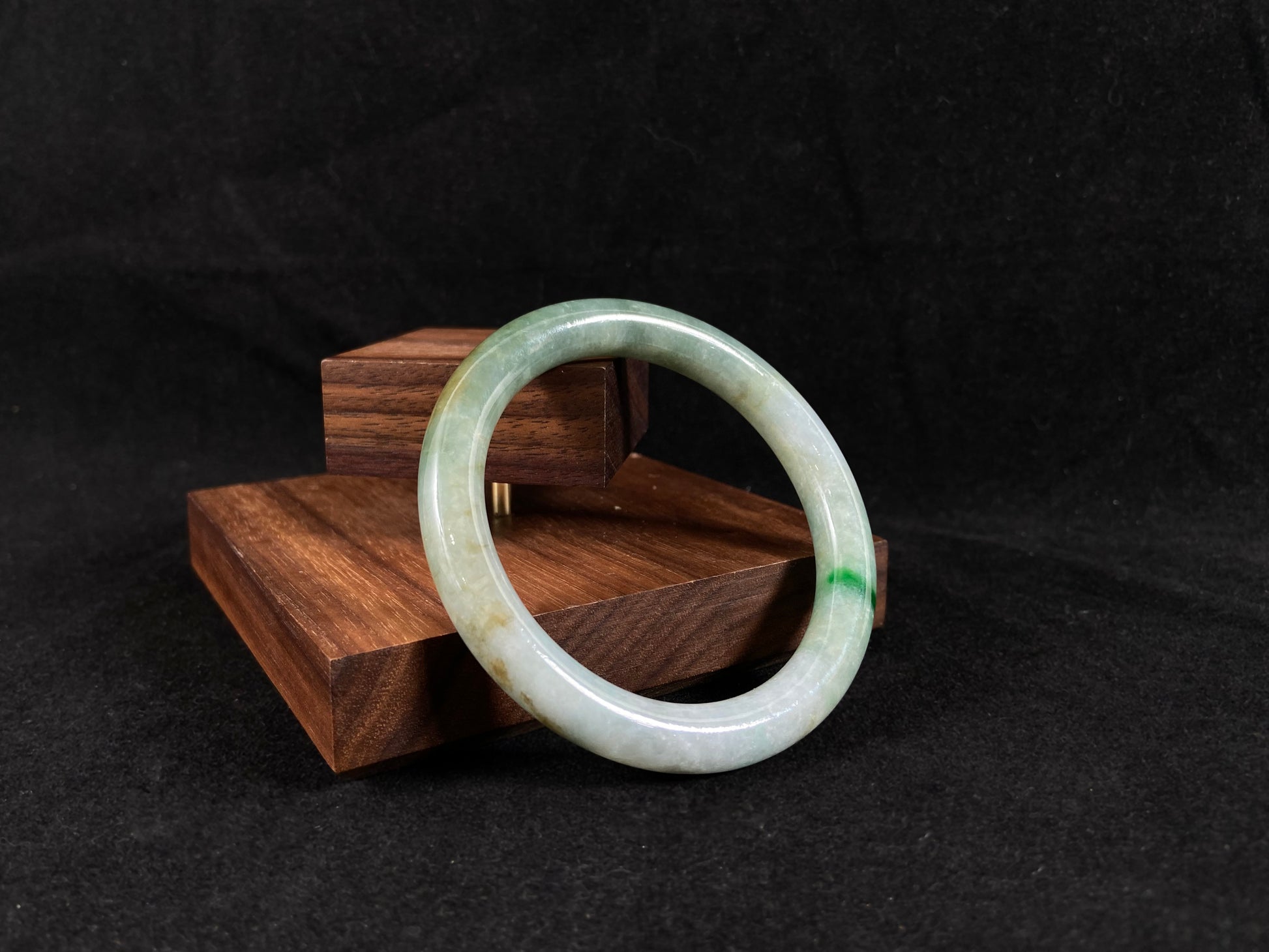 A jade bangle with an emerald vein rests on a white fan inscribed with "Shun Sui".