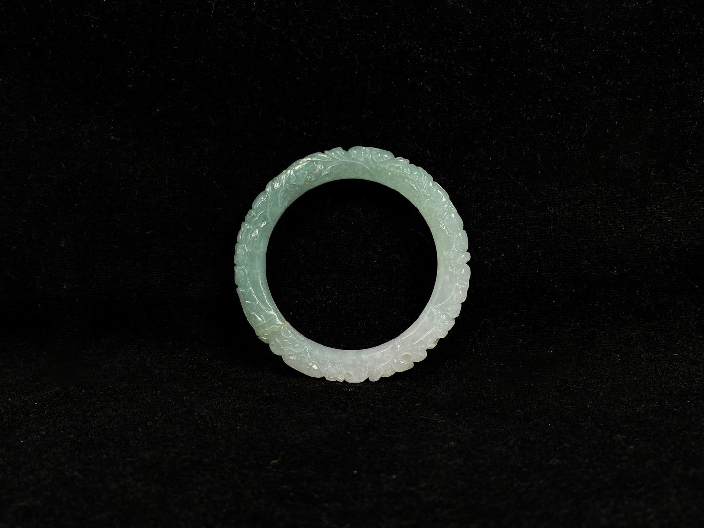A carved jadeite bangle with half green and half white sections.