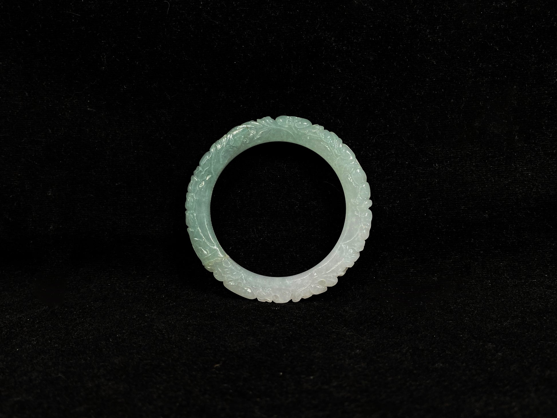 A carved jadeite bangle with half green and half white sections.