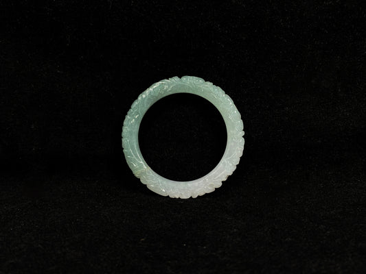 A carved jadeite bangle with half green and half white sections.