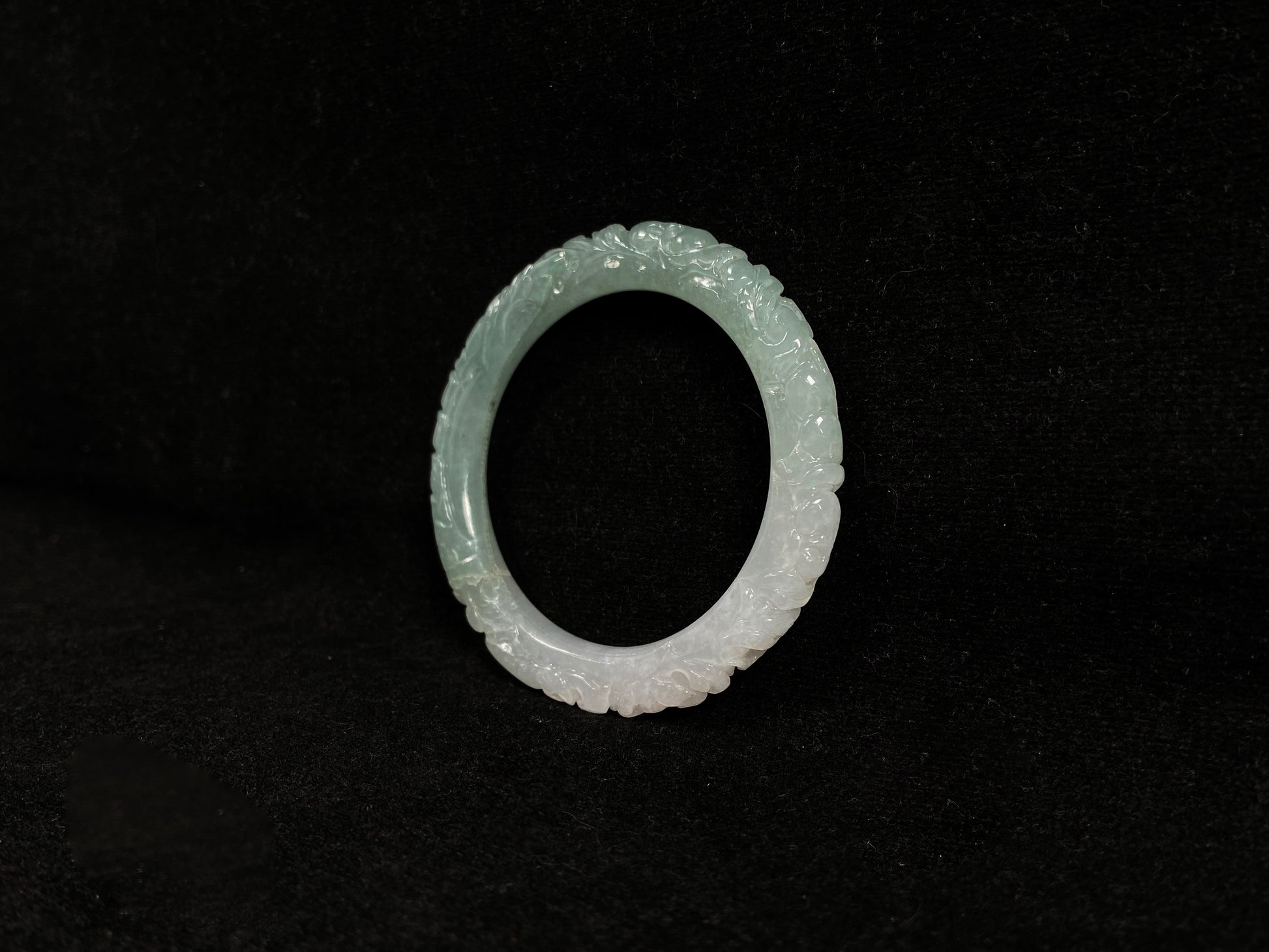 A carved jadeite bangle with half green and half white sections.