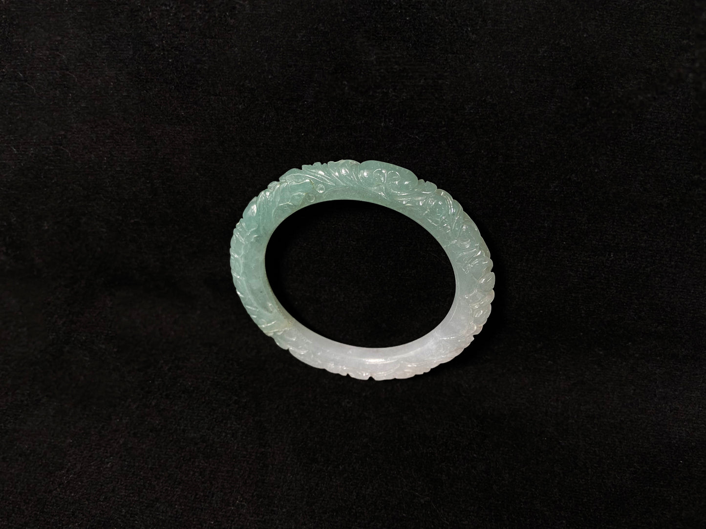 A carved jadeite bangle with half green and half white sections.