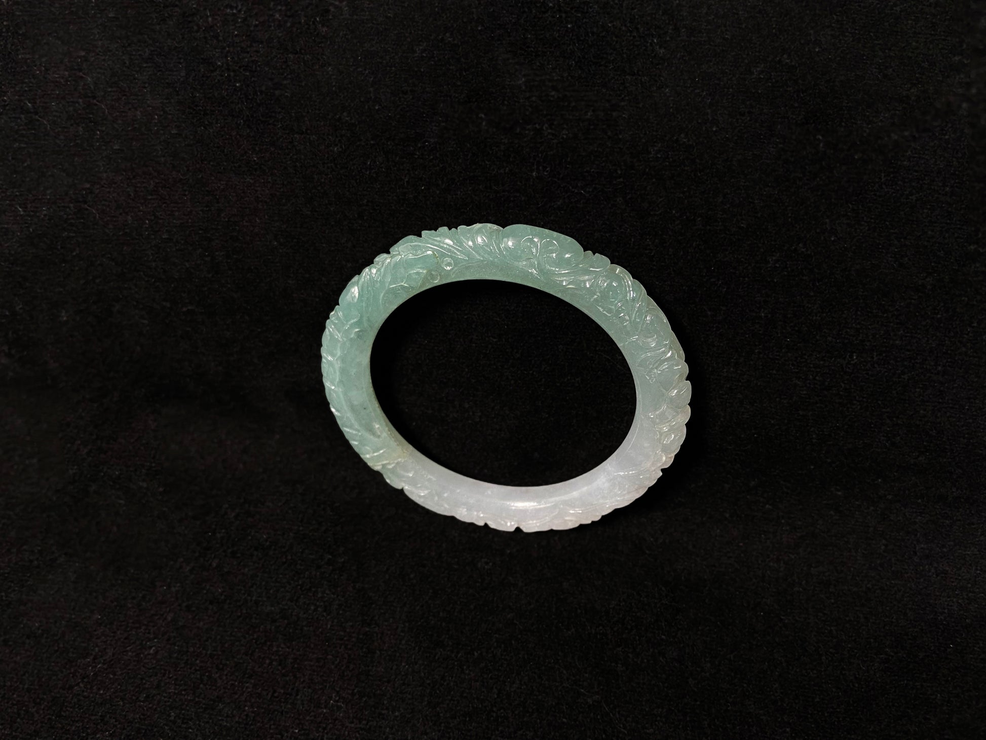 A carved jadeite bangle with half green and half white sections.