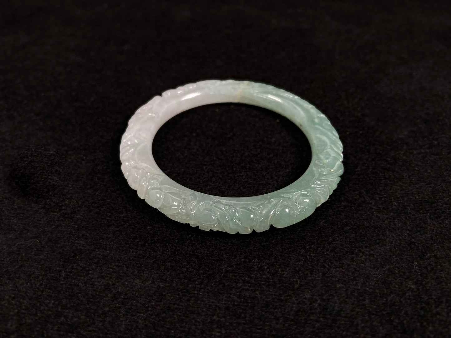 A carved jadeite bangle with half green and half white sections.