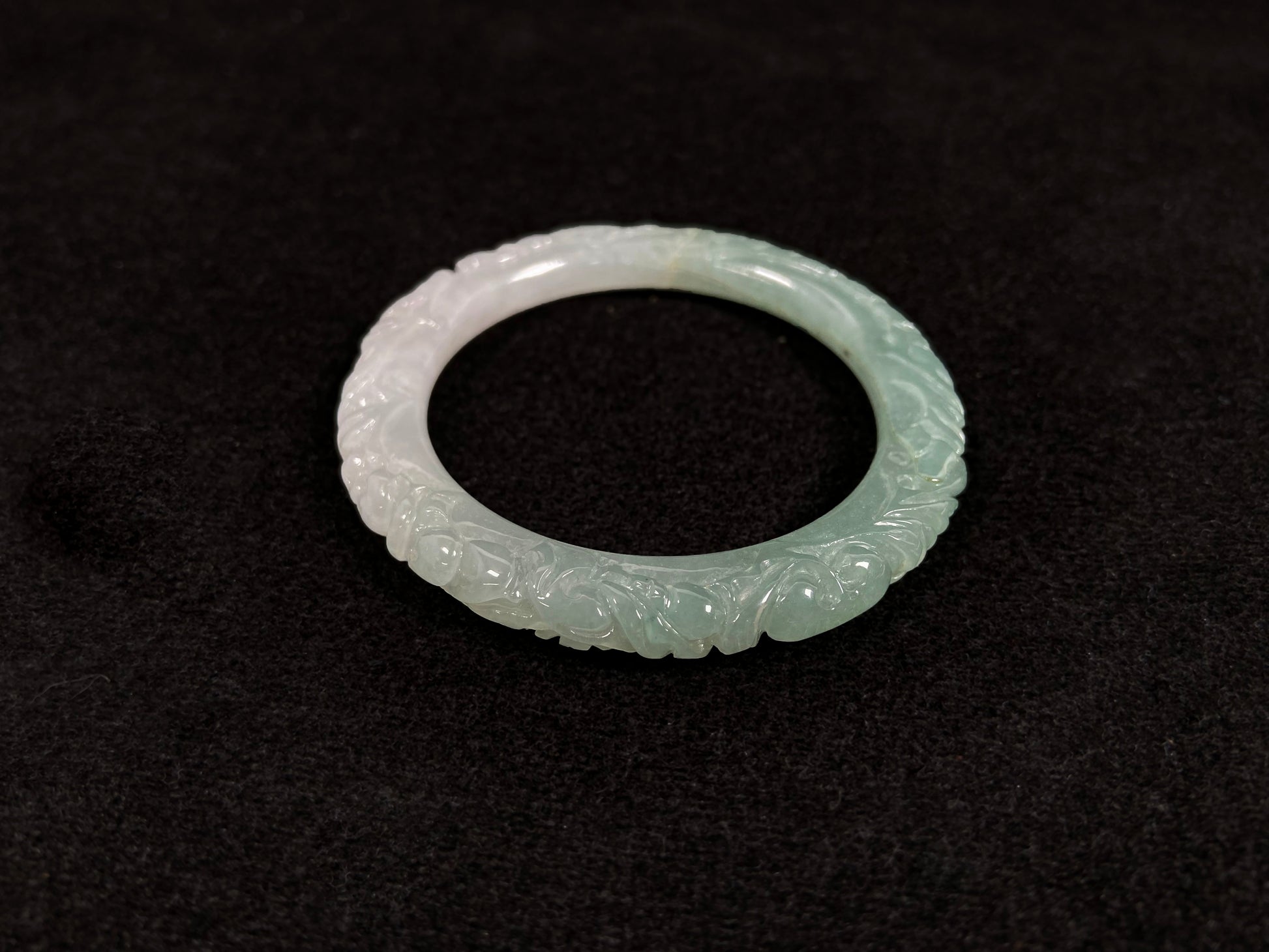 A carved jadeite bangle with half green and half white sections.