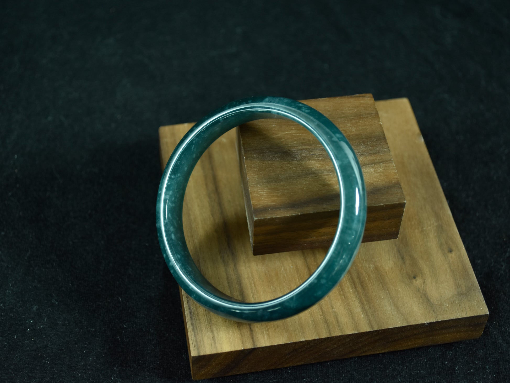 Green jade ring on a wooden stand against a dark background