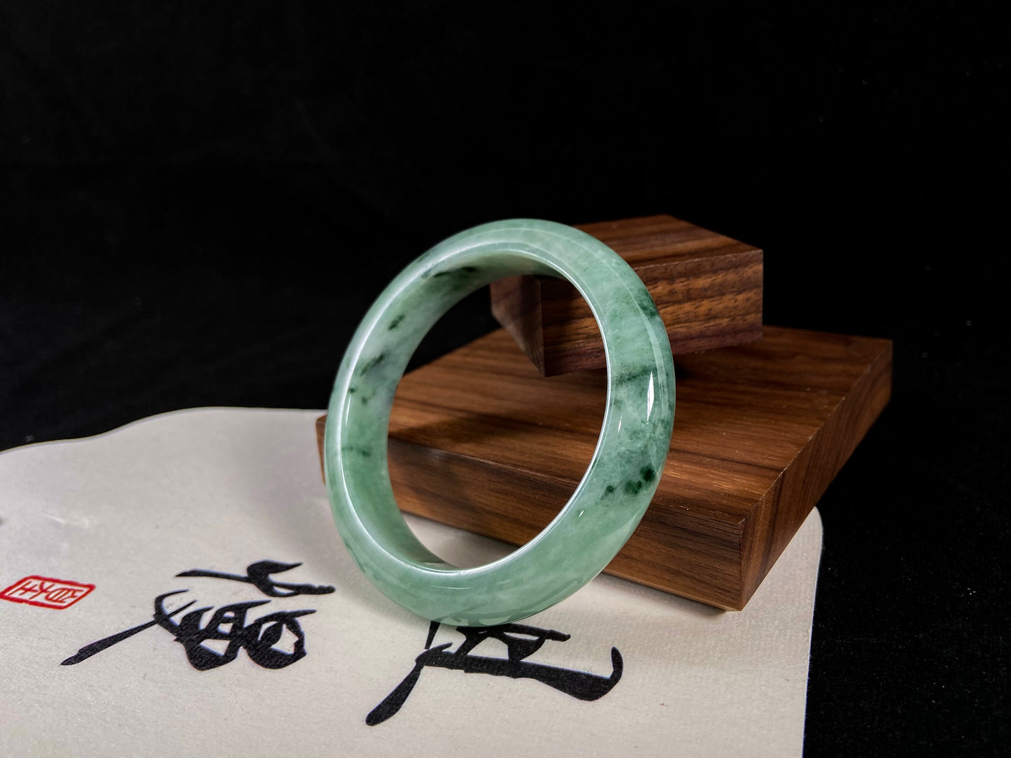 Green jade bracelet on a wooden stand with calligraphy on a white background