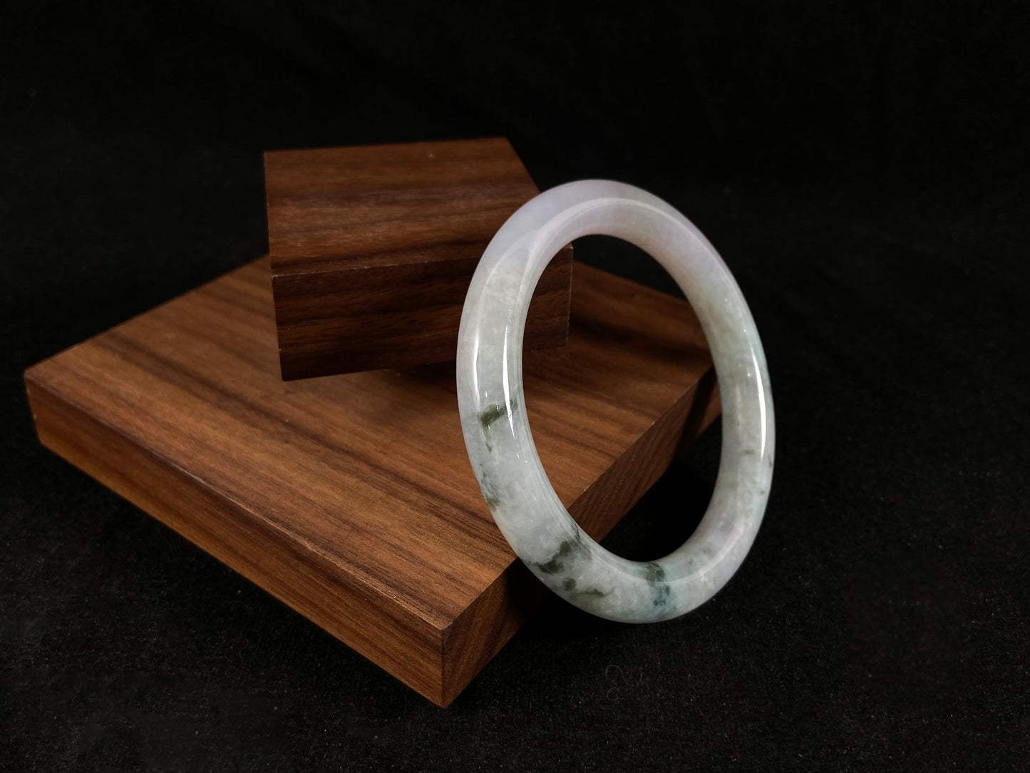 Jade bangle beside wooden planks highlights moss green and ivory veins.