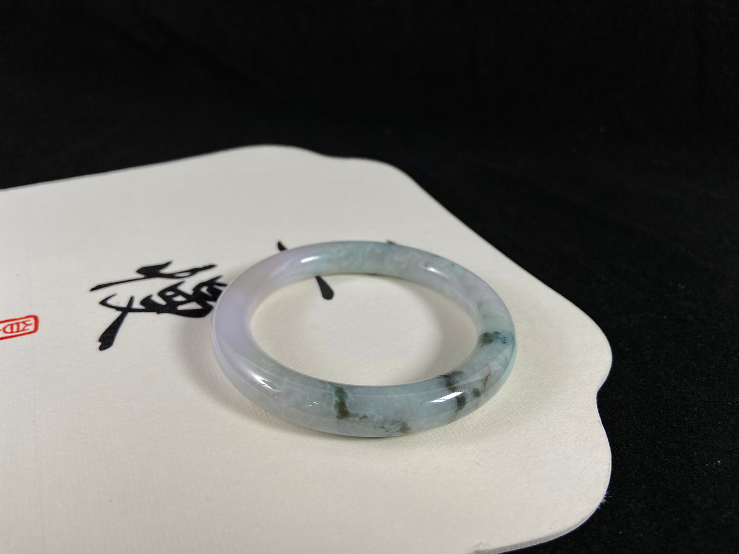 Perched upon a white fan, the jade bangle unveils its striking contrast of ink-green and cloud-white veins.