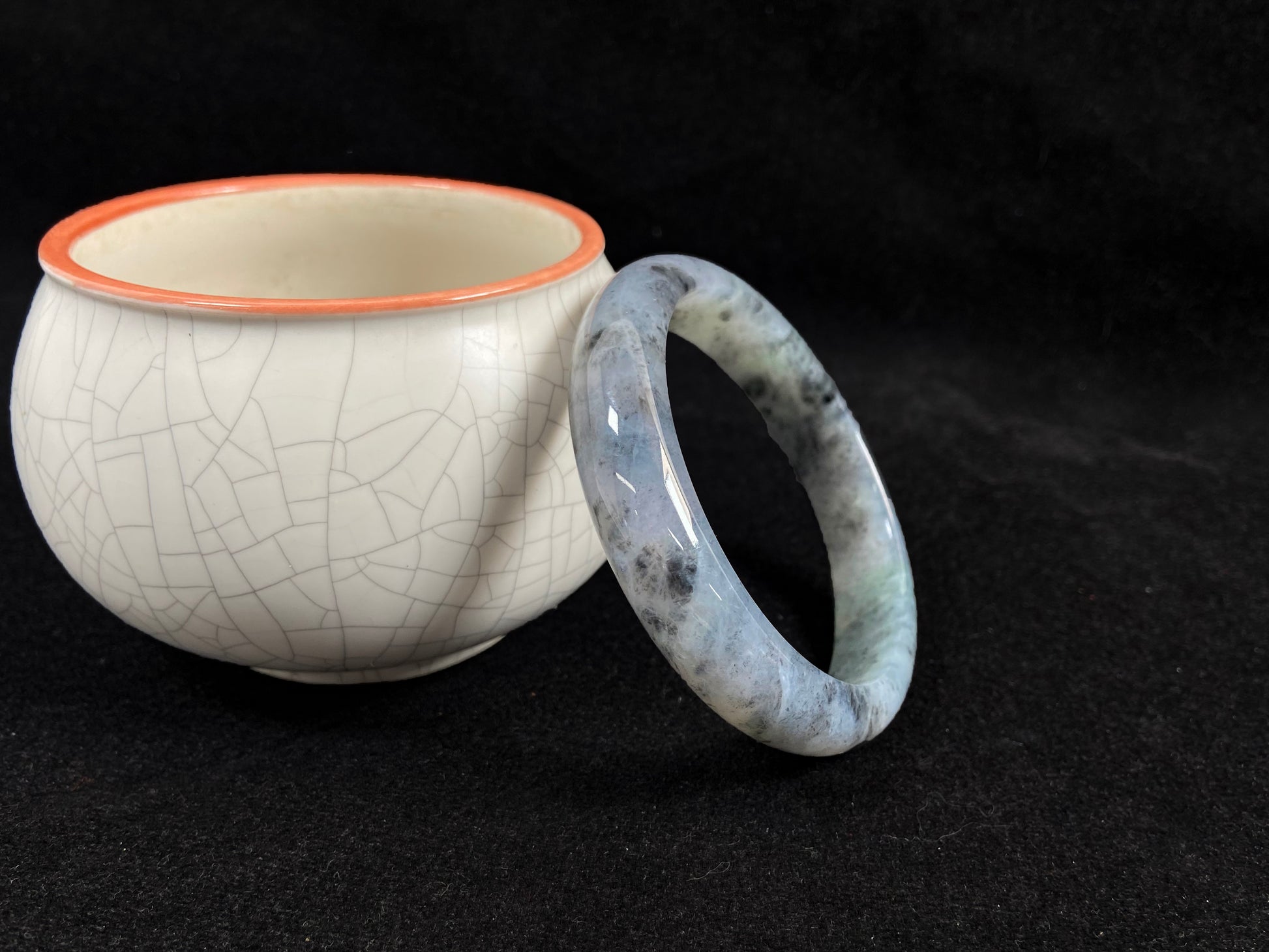 This jadeite bangle features a semi-transparent light green base with evenly distributed charcoal grey inclusions.