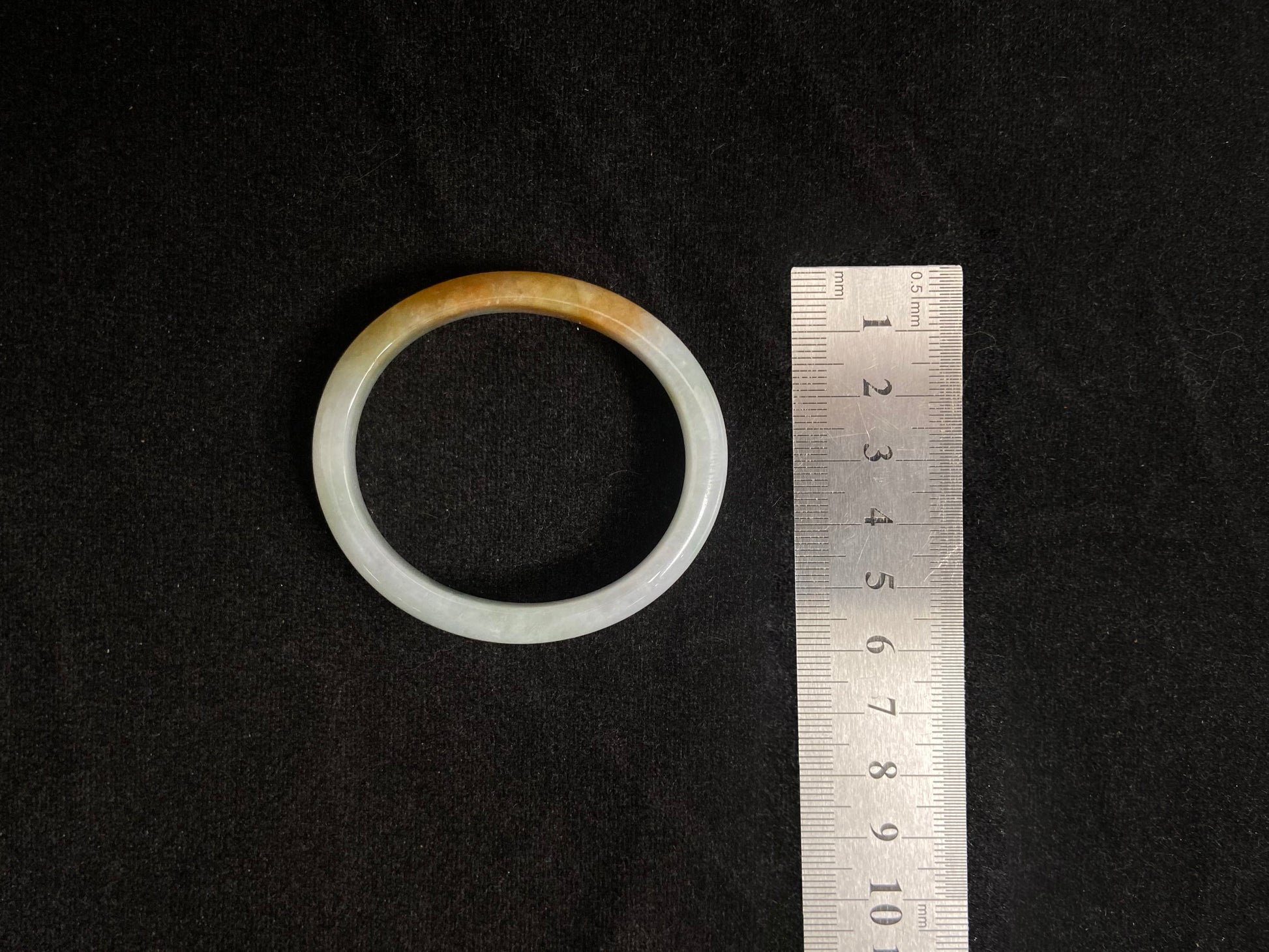 This jade bangle features a creamy white base adorned with delicate gold sprinkles, creating an elegant two tone effect.