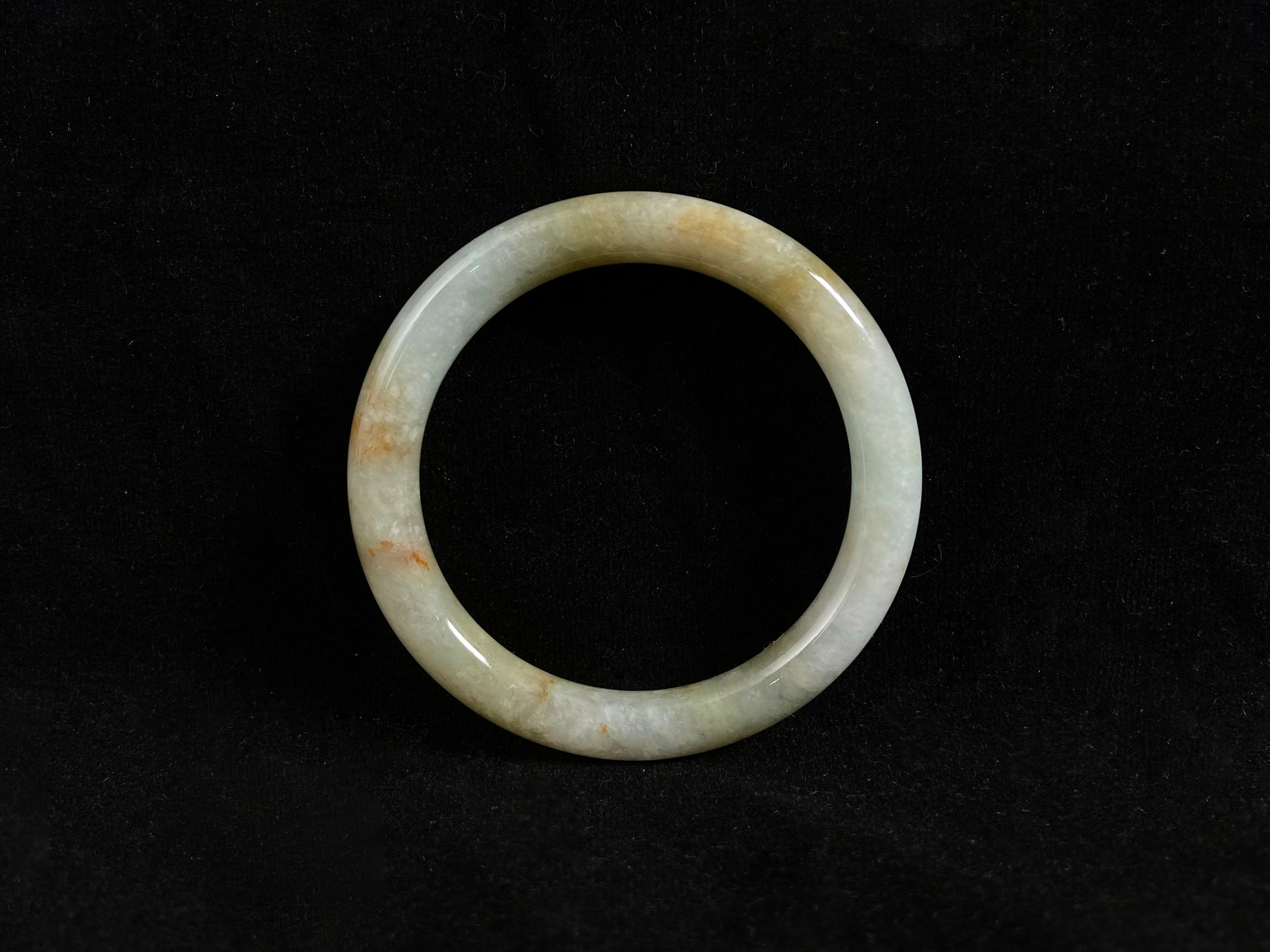 A white and green jade bangle with golden-brown specks, symbolizing harmony and fulfillment