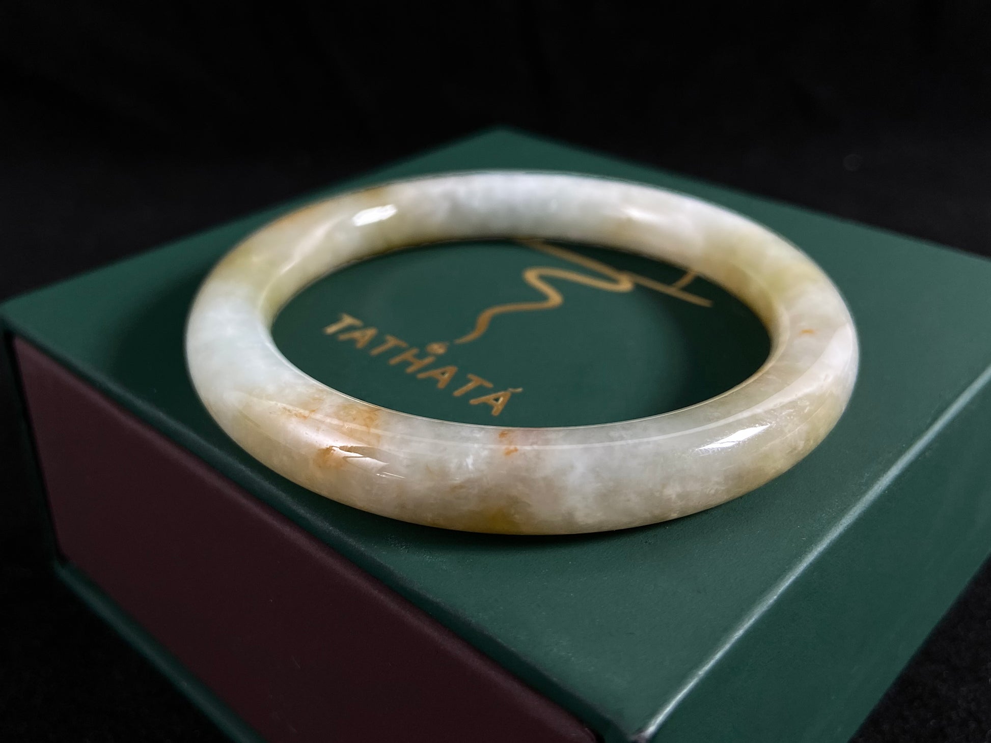 A white and green jade bangle with golden-brown specks, symbolizing harmony and fulfillment