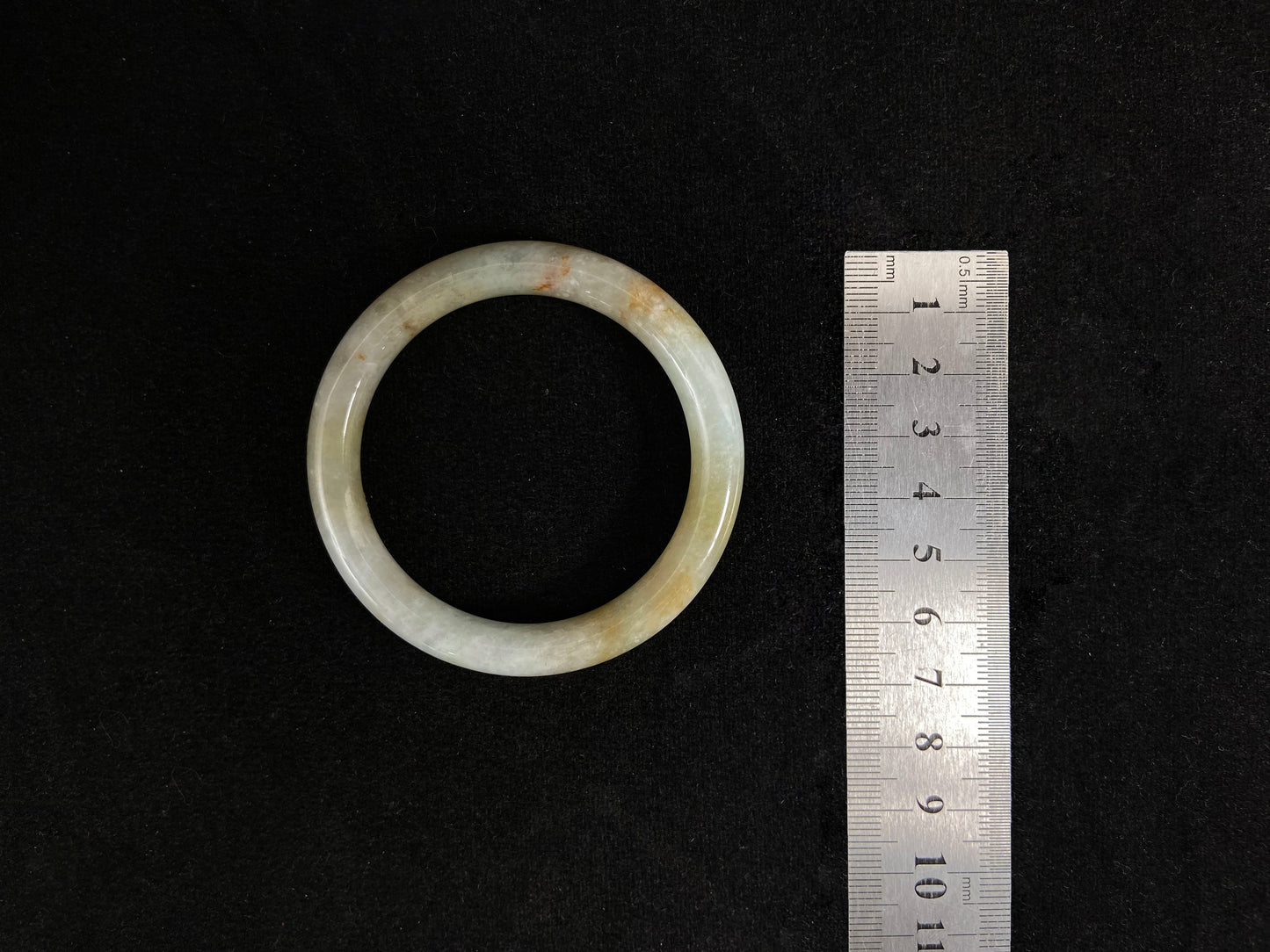 A white and green jade bangle with golden-brown specks, symbolizing harmony and fulfillment