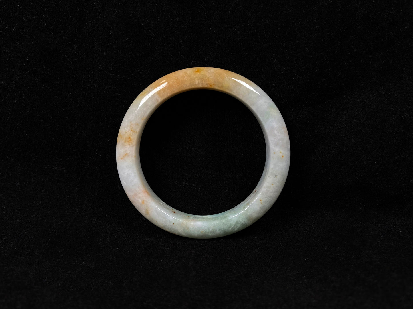 A creamy white jadeite bangle with subtle green undertones and gold sprinkles.