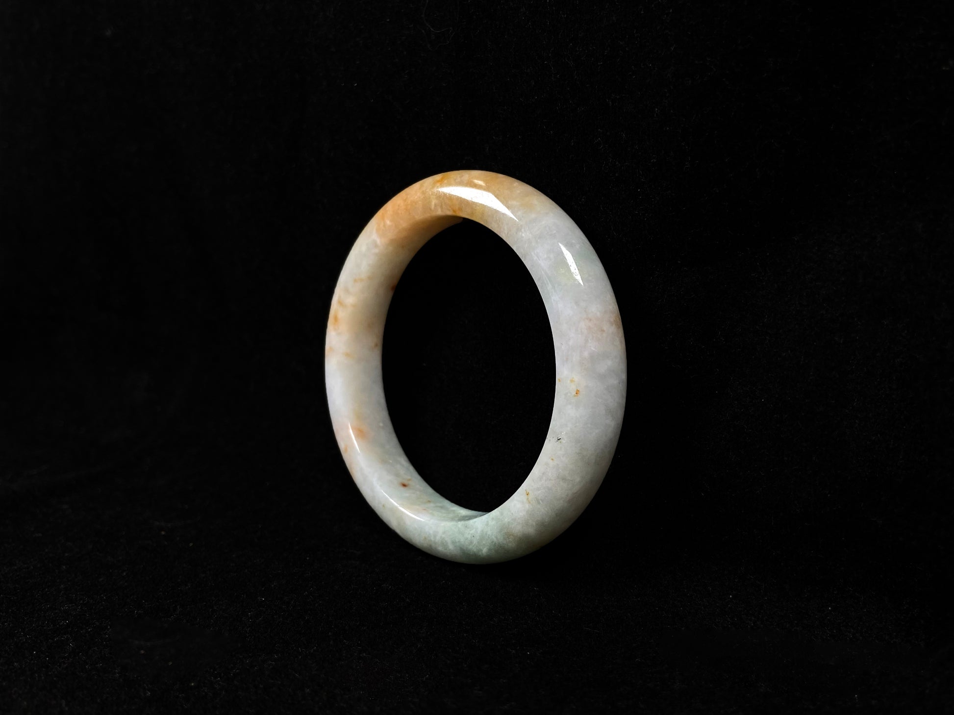 A creamy white jadeite bangle with subtle green undertones and gold sprinkles.