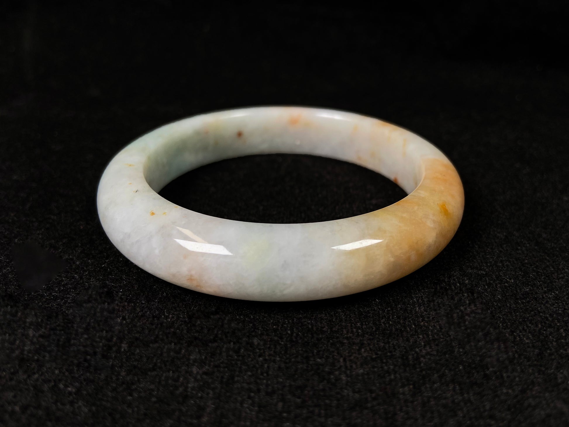 A creamy white jadeite bangle with subtle green undertones and gold sprinkles.