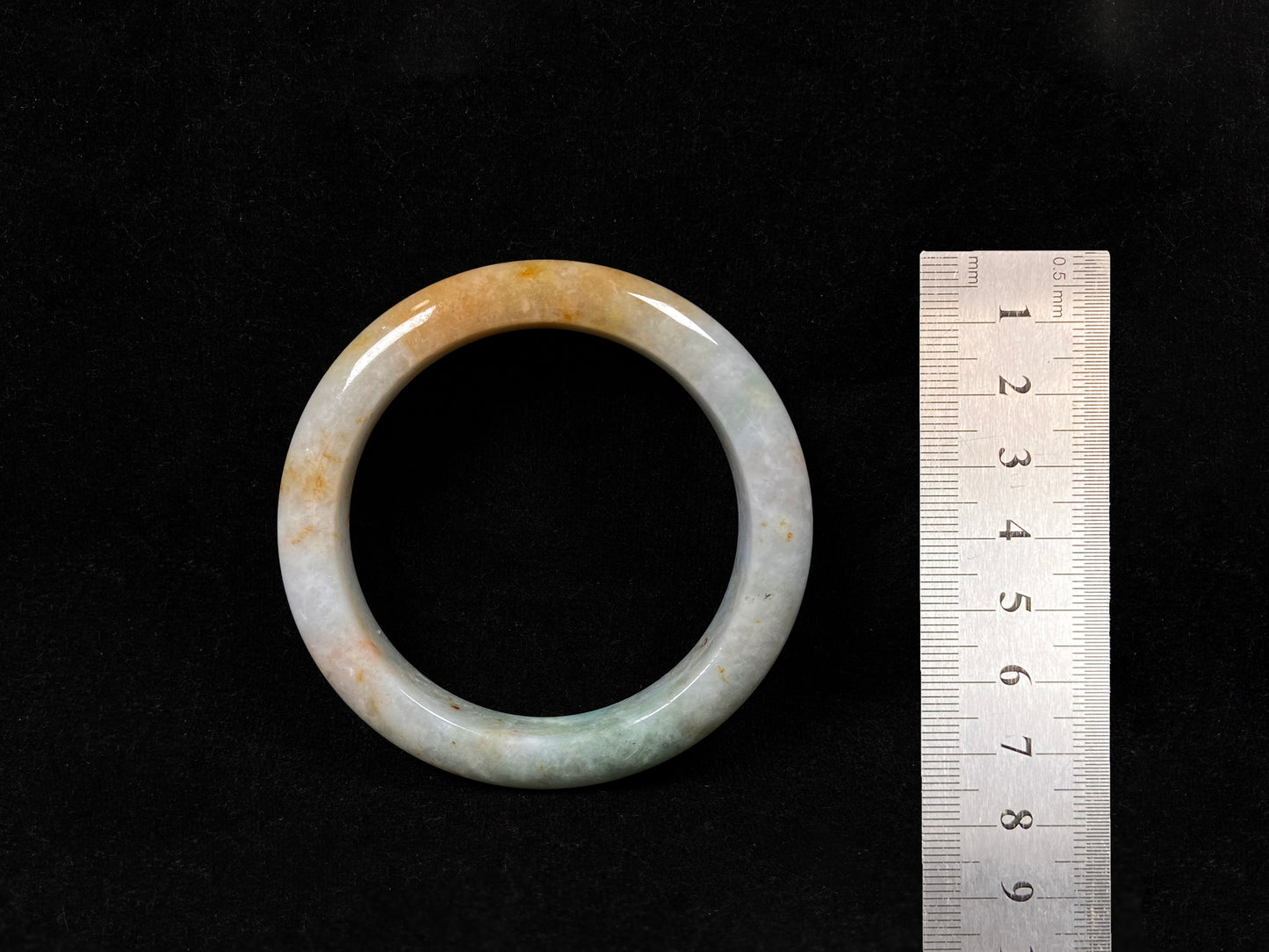 A creamy white jadeite bangle with subtle green undertones and gold sprinkles.