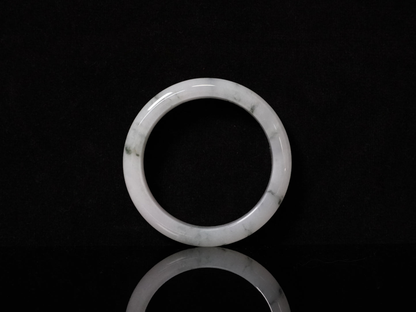 This jadeite bangle features a milky base adorned with delicate ink-wash veining.