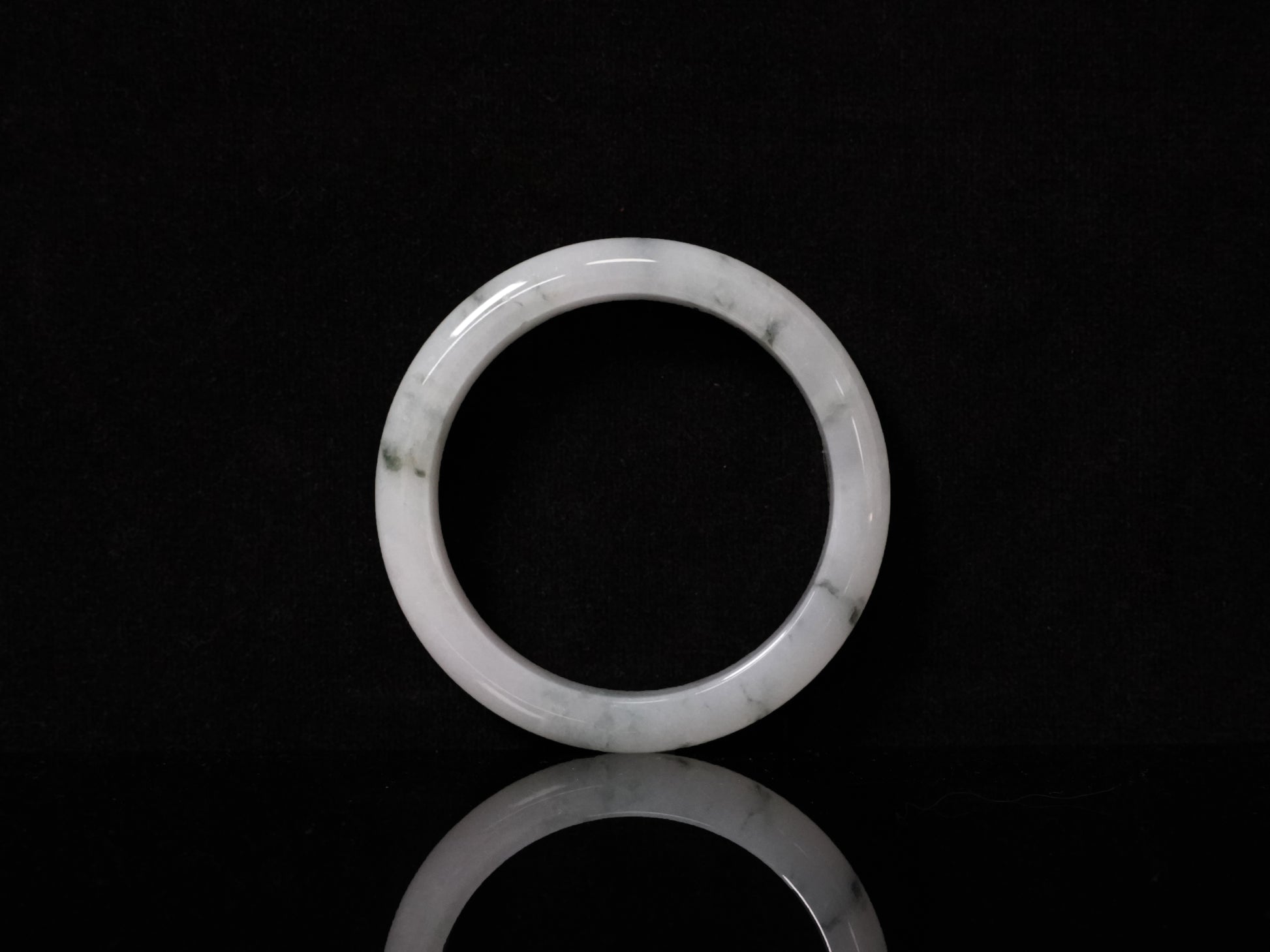 This jadeite bangle features a milky base adorned with delicate ink-wash veining.