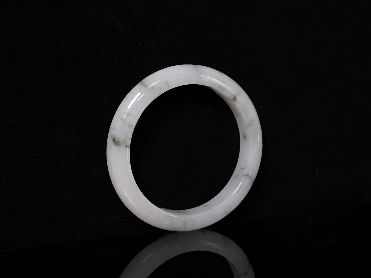 This jadeite bangle features a milky base adorned with delicate ink-wash veining.